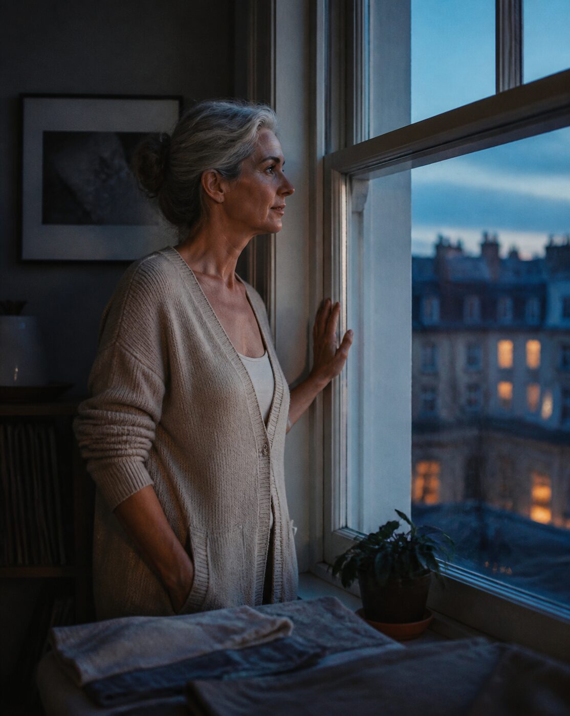 Mujer contemplativa mirando por la ventana de su apartamento a la hora azul